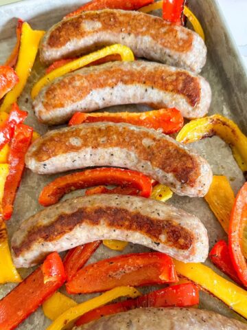 Baked Italian sausages on a baking sheet with cooked bell peppers.