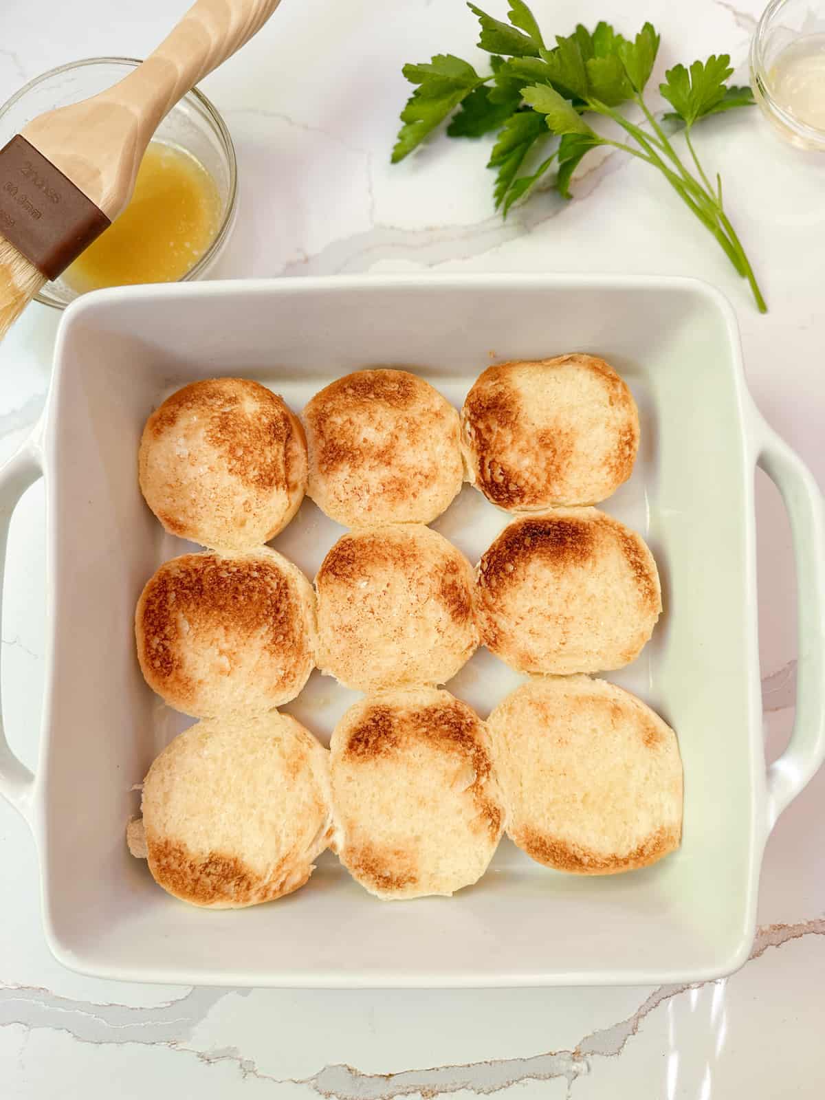 Buttered and toasted slider buns in a pan.