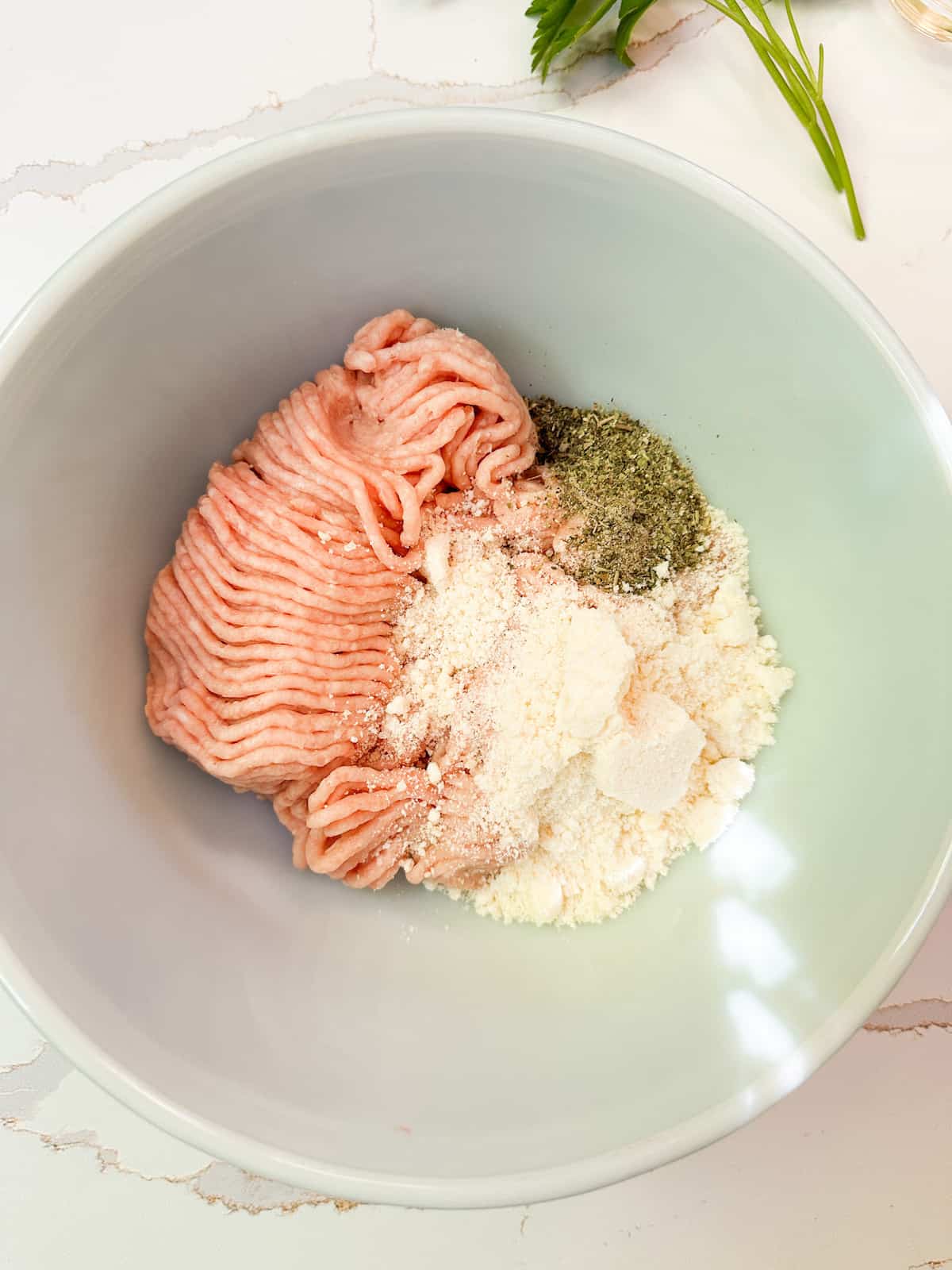 A mixing bowl with ground chicken, Italian seasonings and Parmesan cheese.