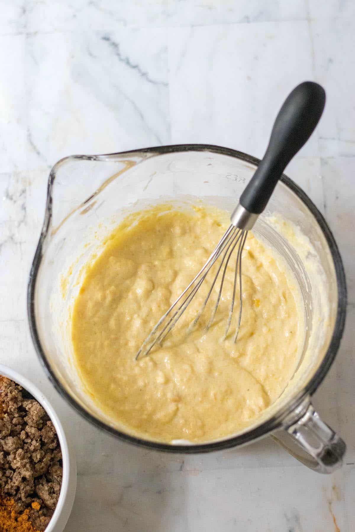 A combined mixture of cornbread mix, creamed corn, sour cream and egg in a mixing bowl.