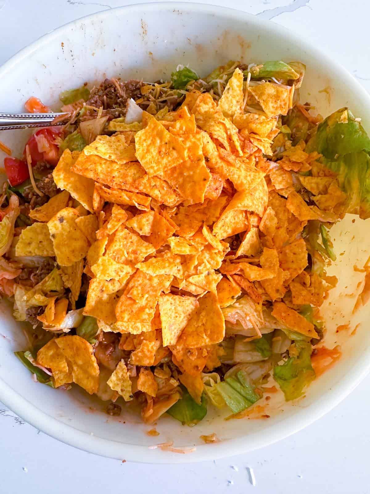 Crushed nacho chips on top of a taco salad.