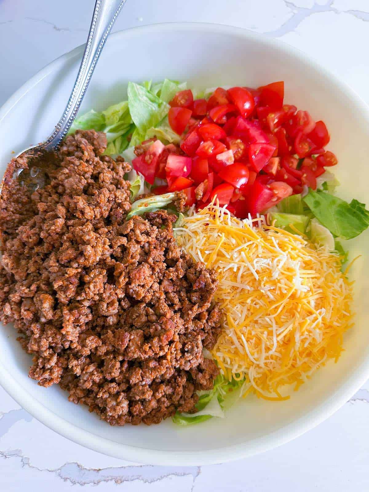 Taco meat, lettuce, cheese blend and diced tomatoes in a mixing bowl.