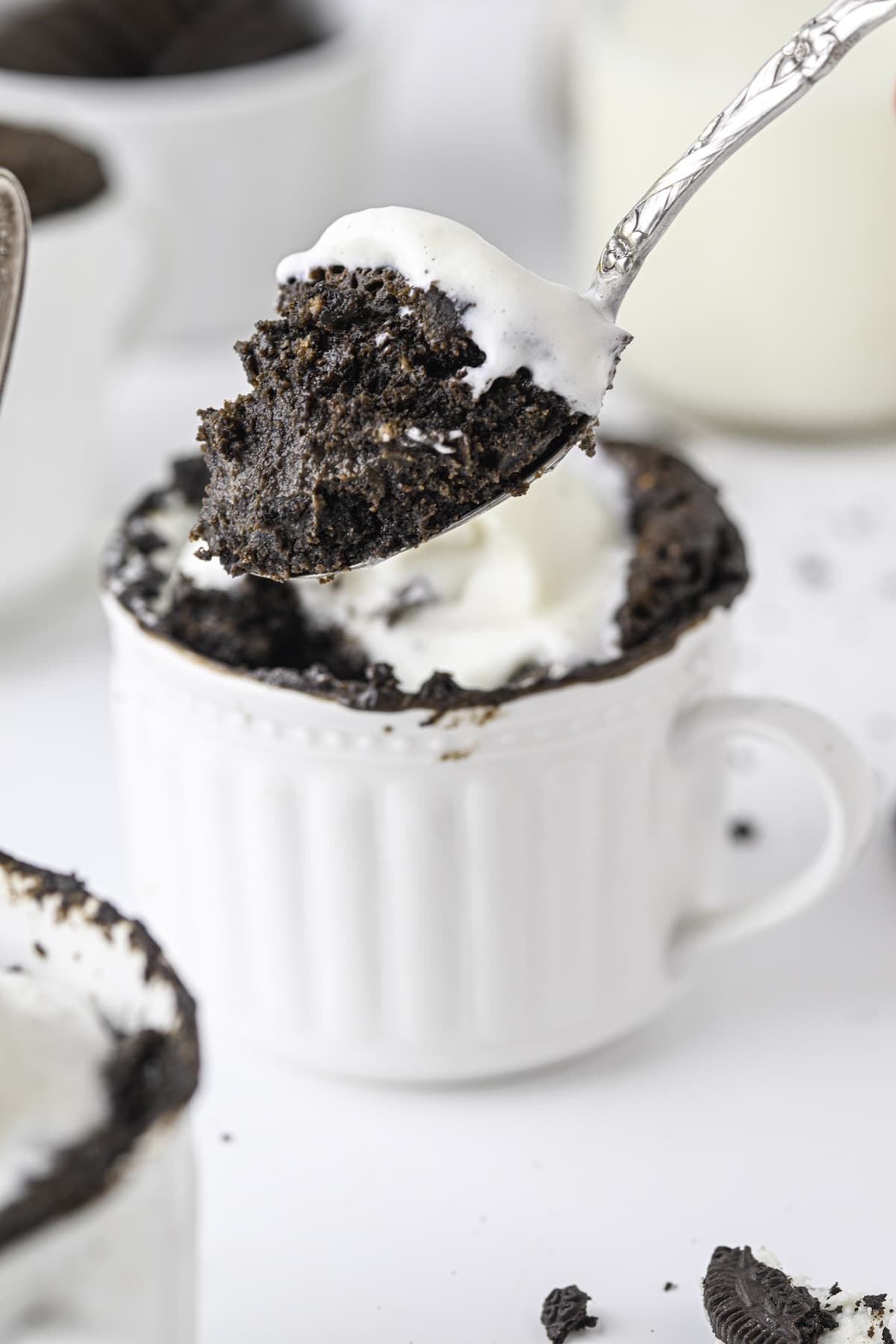 A spoonful of oreo cake in a cup, topped with vanilla ice cream.