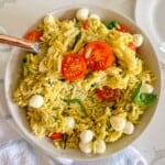 Pesto pasta salad with a serving taken out of it and a large spoon.