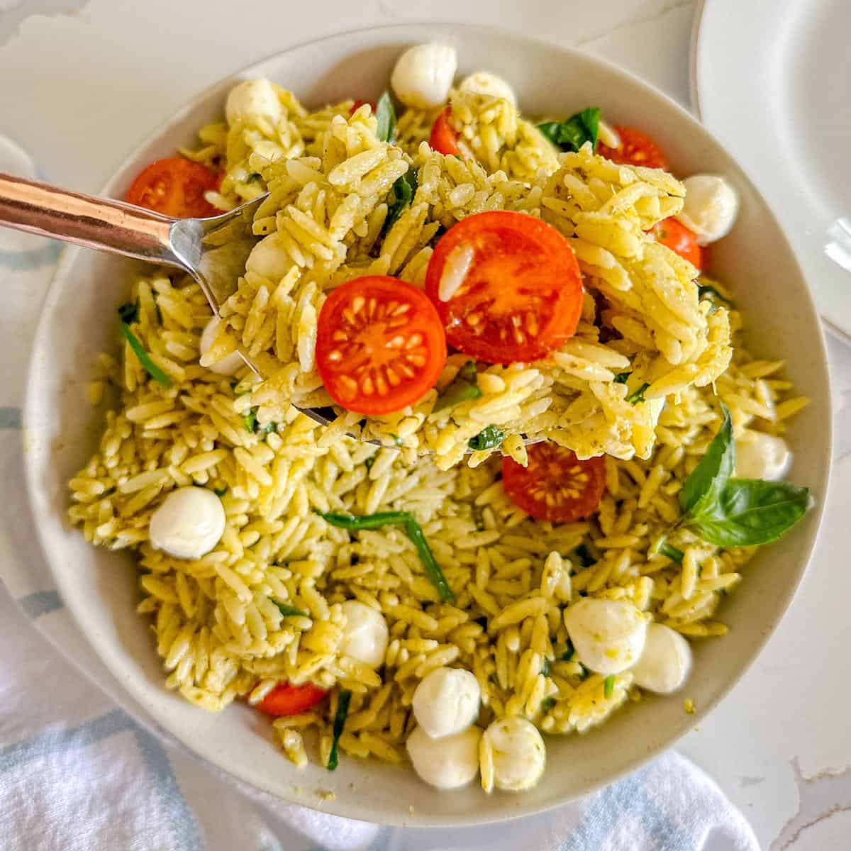 Pesto pasta salad with a serving taken out of it and a large spoon.