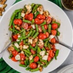 Chopped asparagus with a balsamic dressing, tomatoes, walnuts and feta cheese in a large serving bowl.