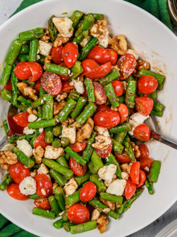 Chopped asparagus with a balsamic dressing, tomatoes, walnuts and feta cheese in a large serving bowl.