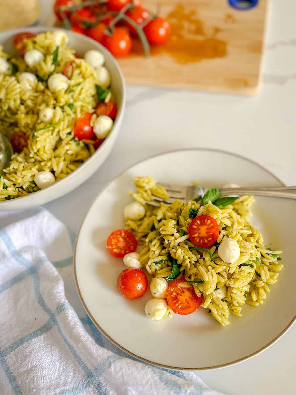 A plate full of orzo pesto salad with a fork.