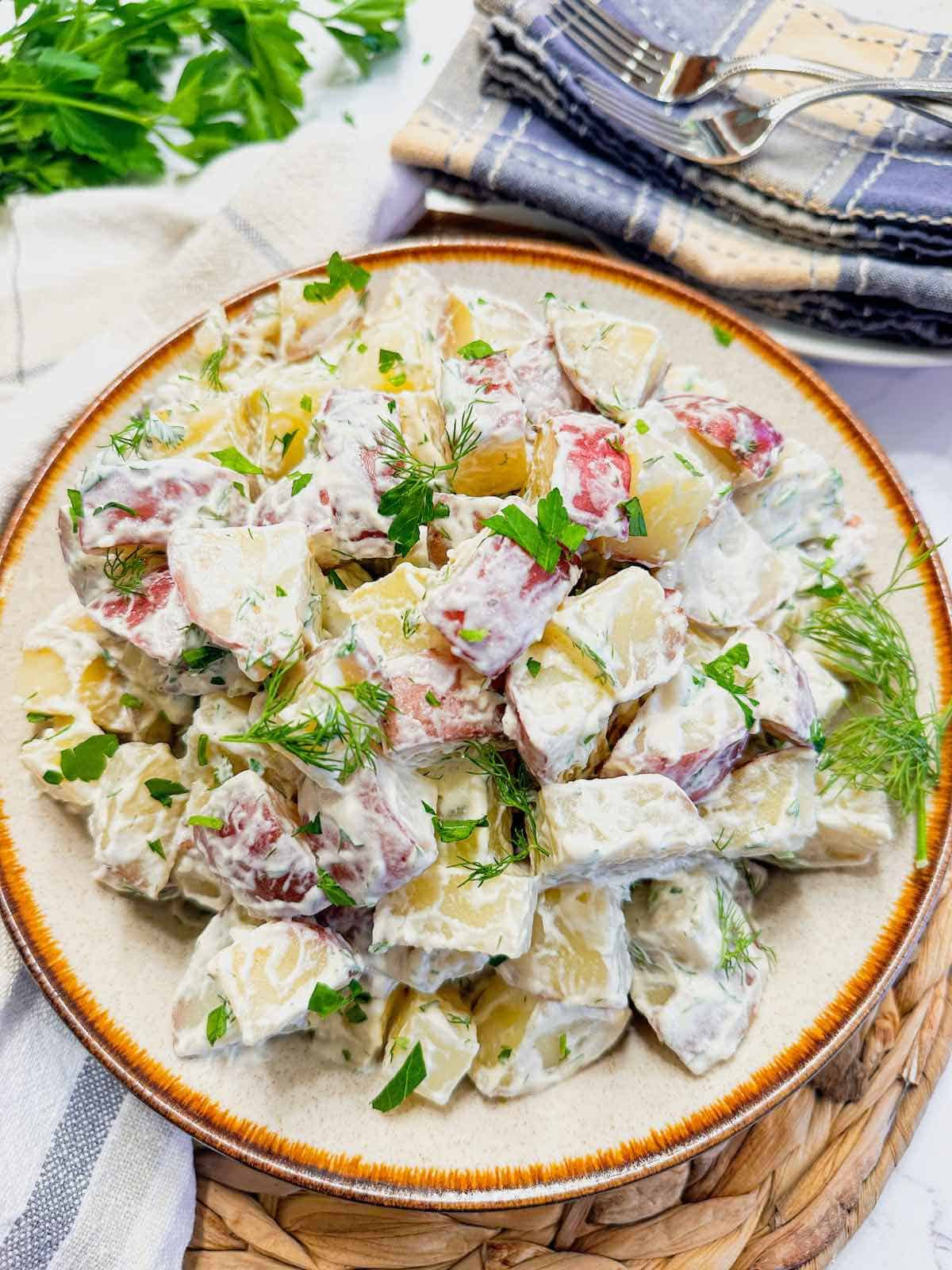 A large bowl of red potato salad topped with fresh dill fronds and chopped parsley.