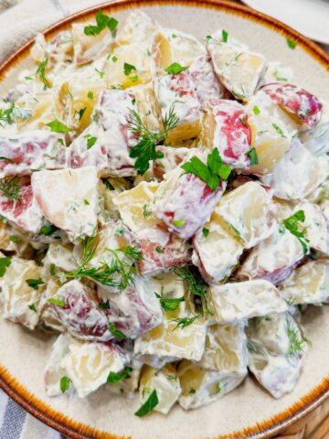 A plate of red potato salad topped with fresh dill.