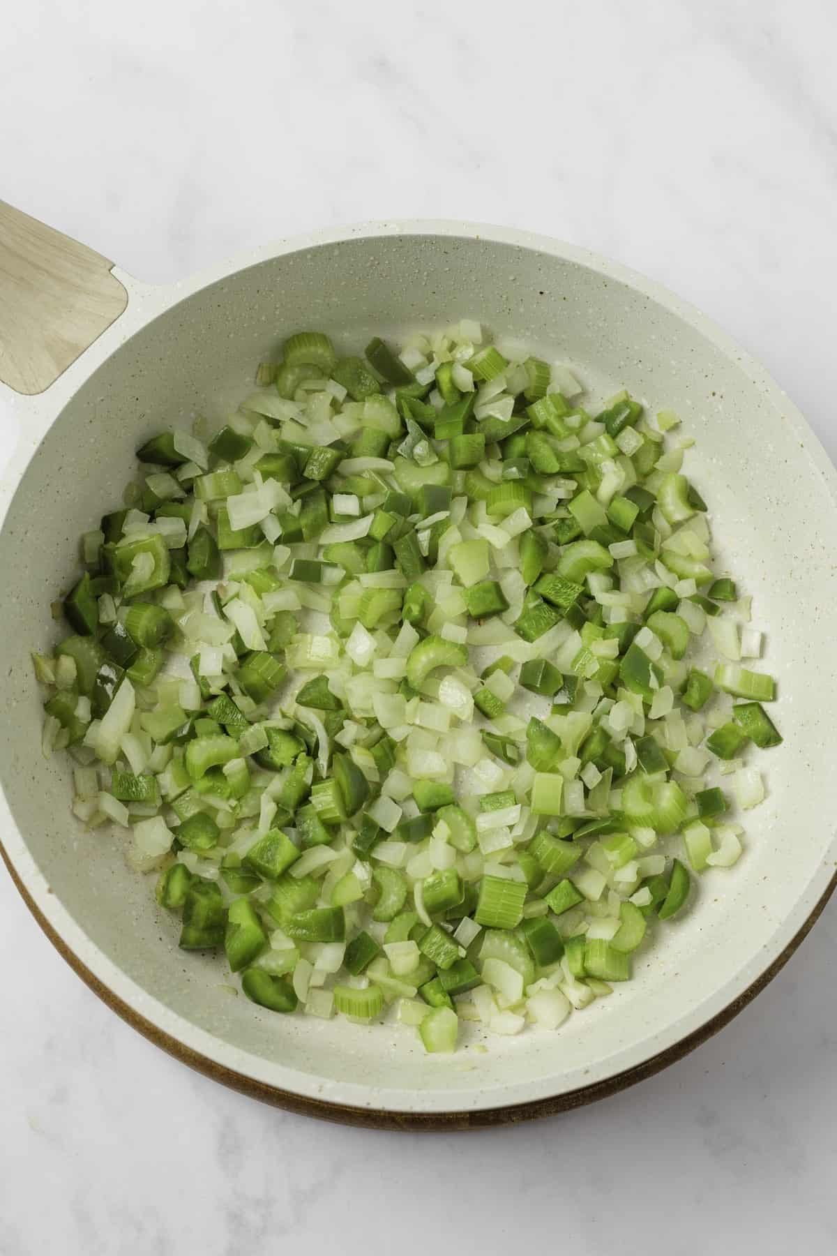 Sautéed celery, onion and green bell pepper in a pan.