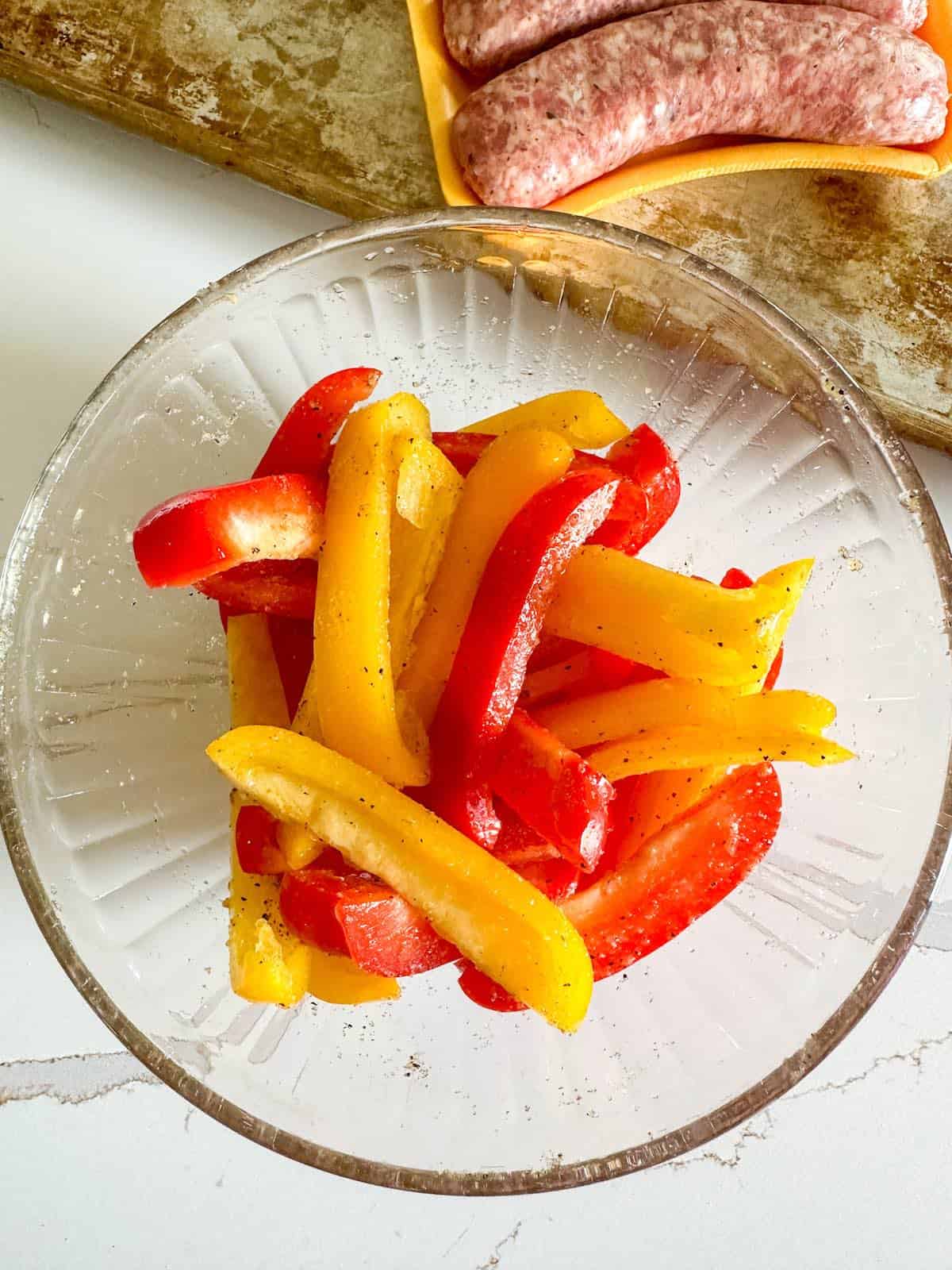 Yellow bell peppers and red bell peppers in a small bowl, tossed in olive oil and spices.