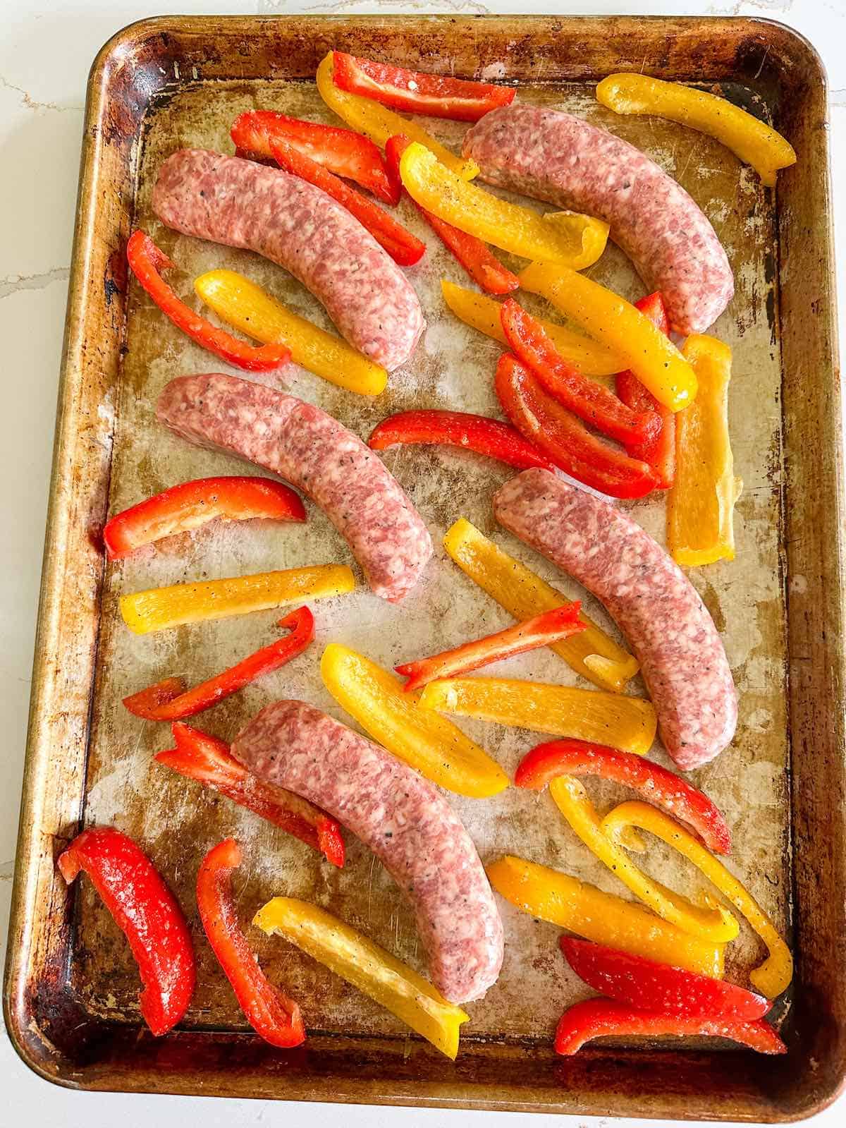 Uncooked Italian sausage and sliced peppers on a baking sheet.