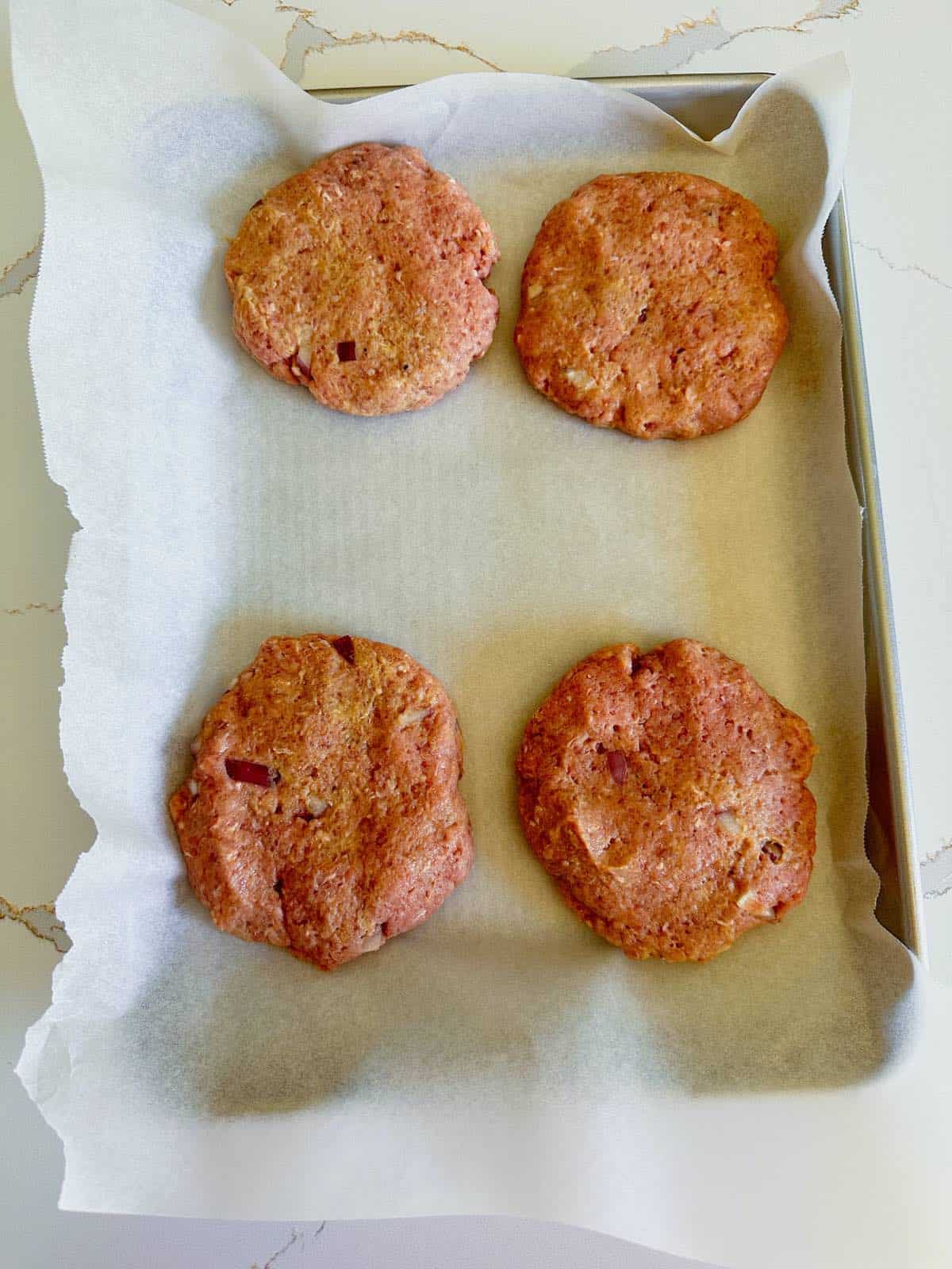 Formed turkey patties on a parchment paper lined baking sheet.