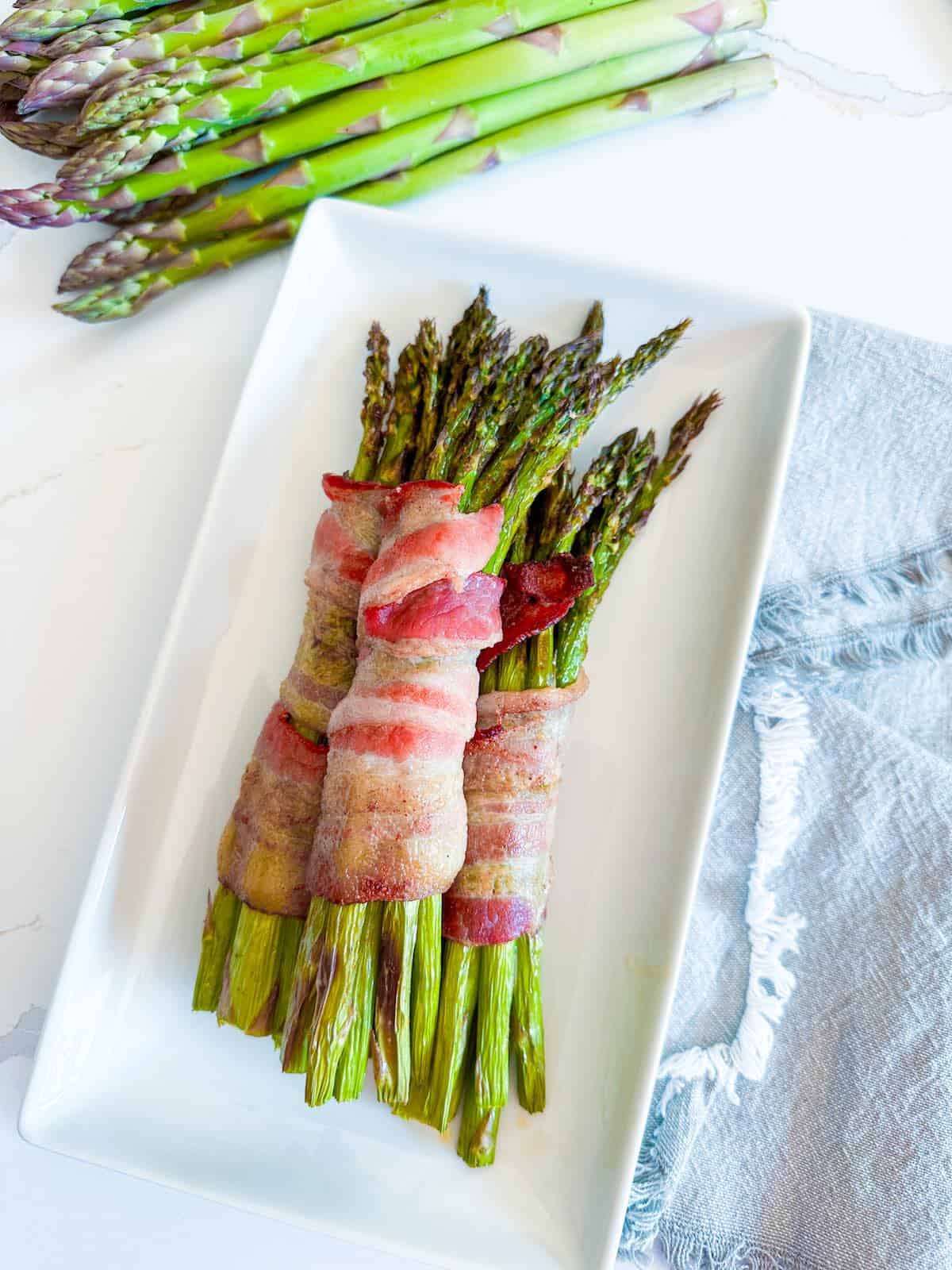 Asparagus spears wrapped in cooked bacon on a plate.