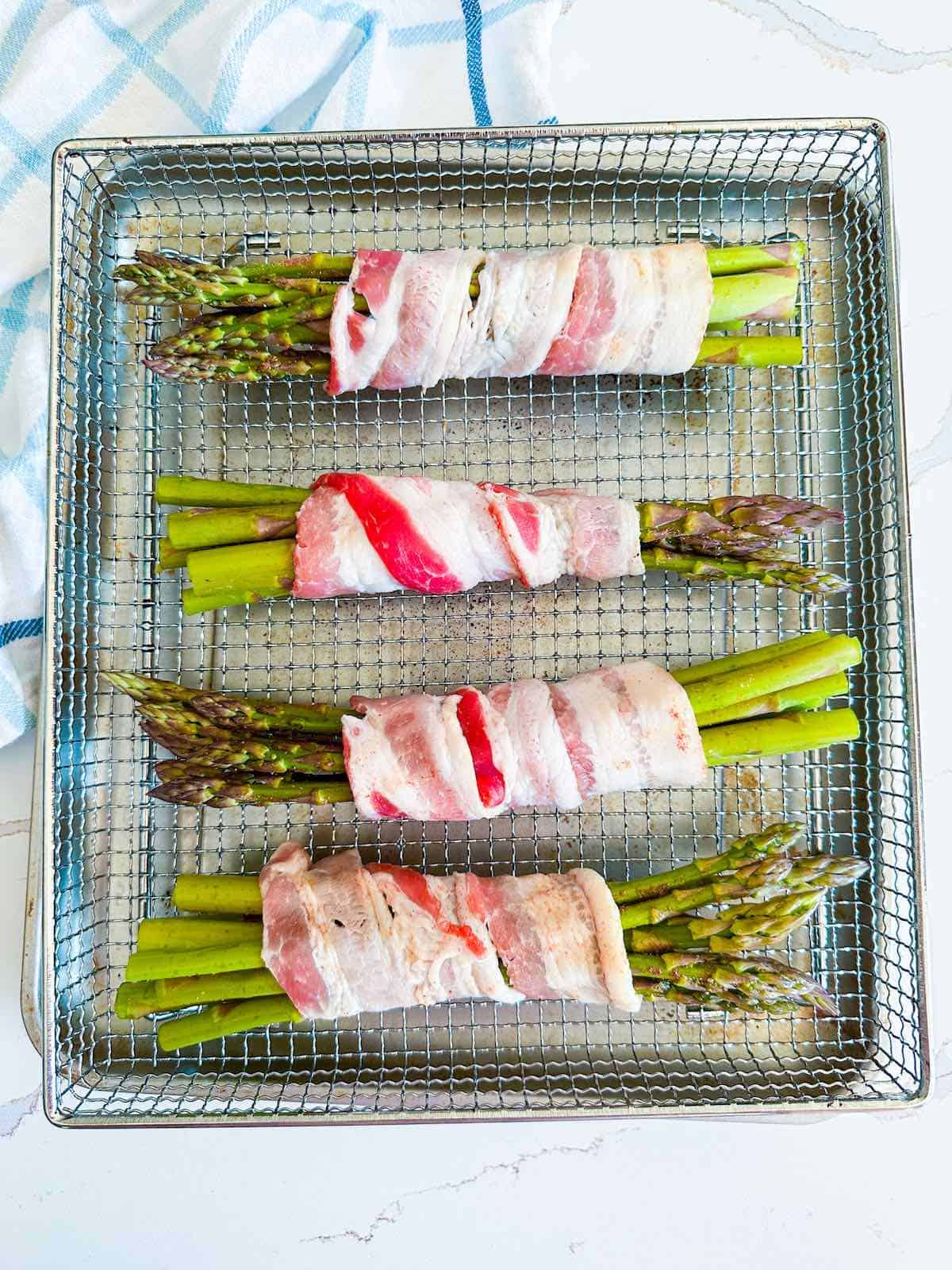 Bacon wrapped asparagus in an air fryer basket before cooking.