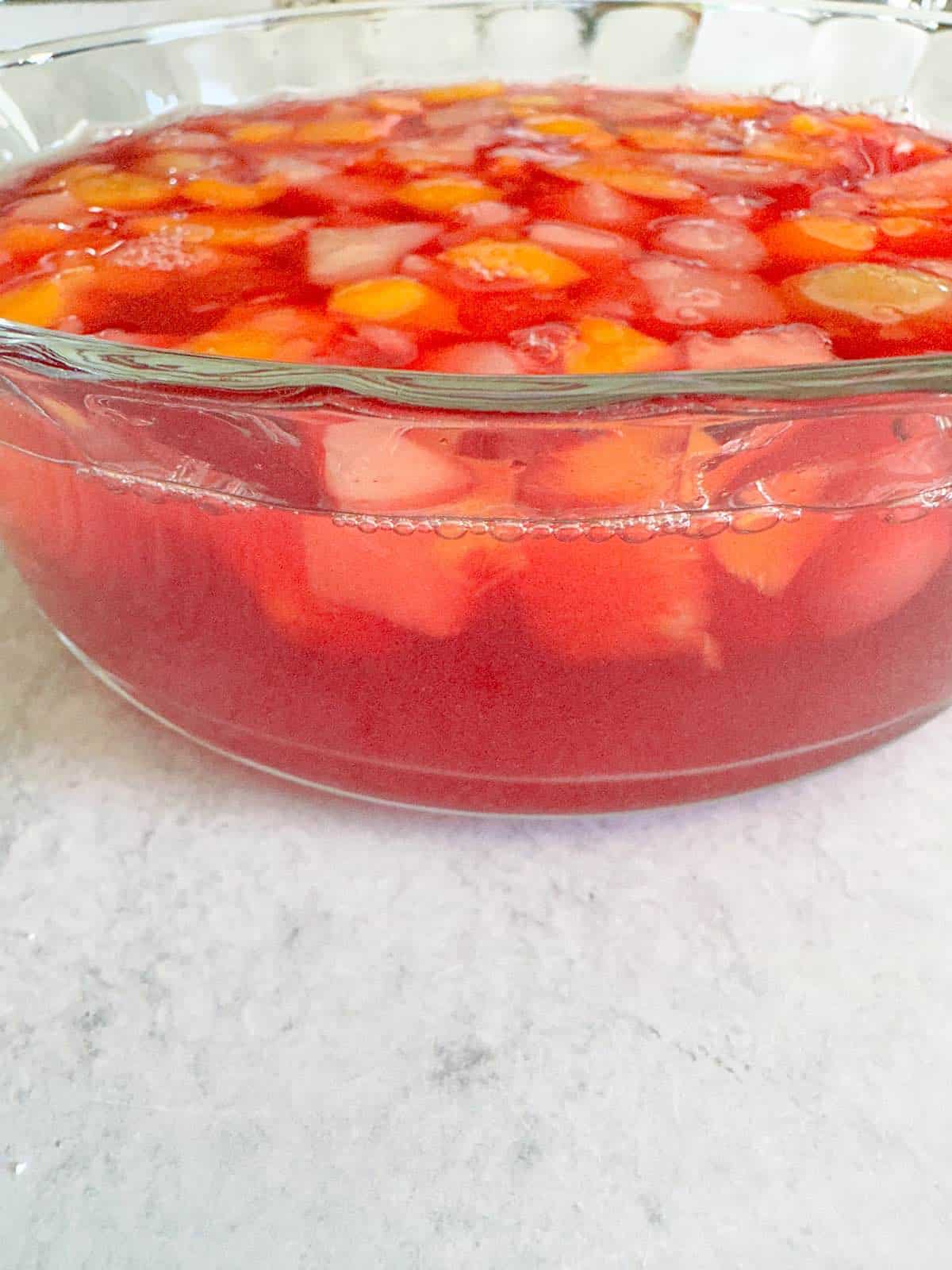 Fruit cocktail in jello in a glass bowl.