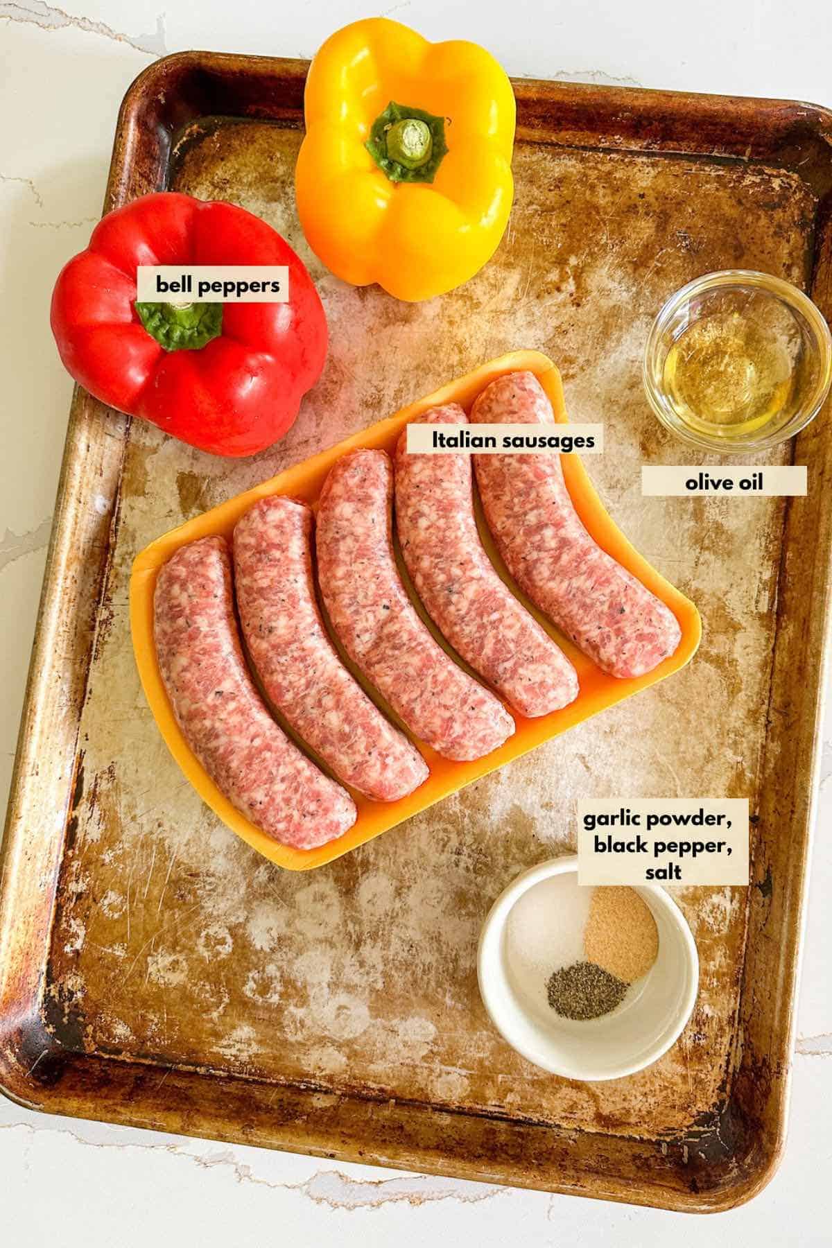 Ingredients on a baking sheet laid out Italian sausages, bell peppers, olive oil, garlic powder, salt and black pepper.