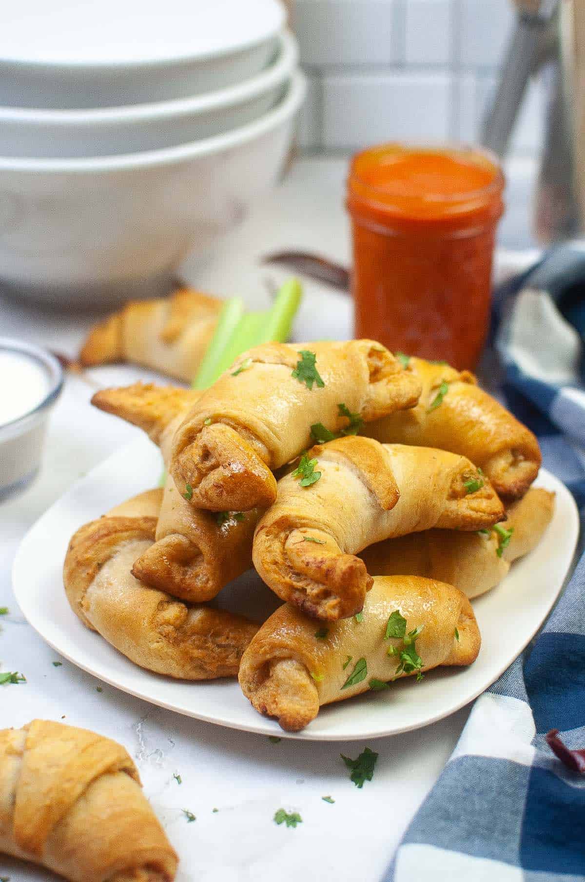 Buffalo sauce on the side of rolled up crescent rolls stuffed with chicken.