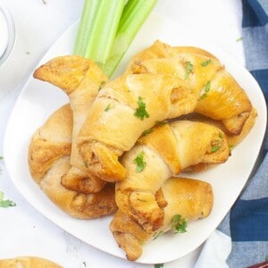 Buffalo chicken crescent rolls stacked on a plate with celery sticks.