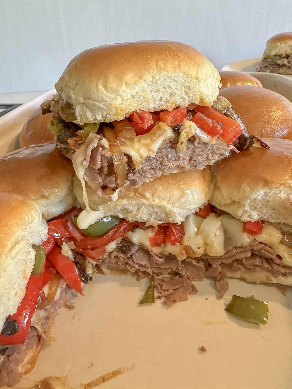 Stacked philly cheesesteak sliders with roast beef and peppers with ingredients spilling out and melted cheese.