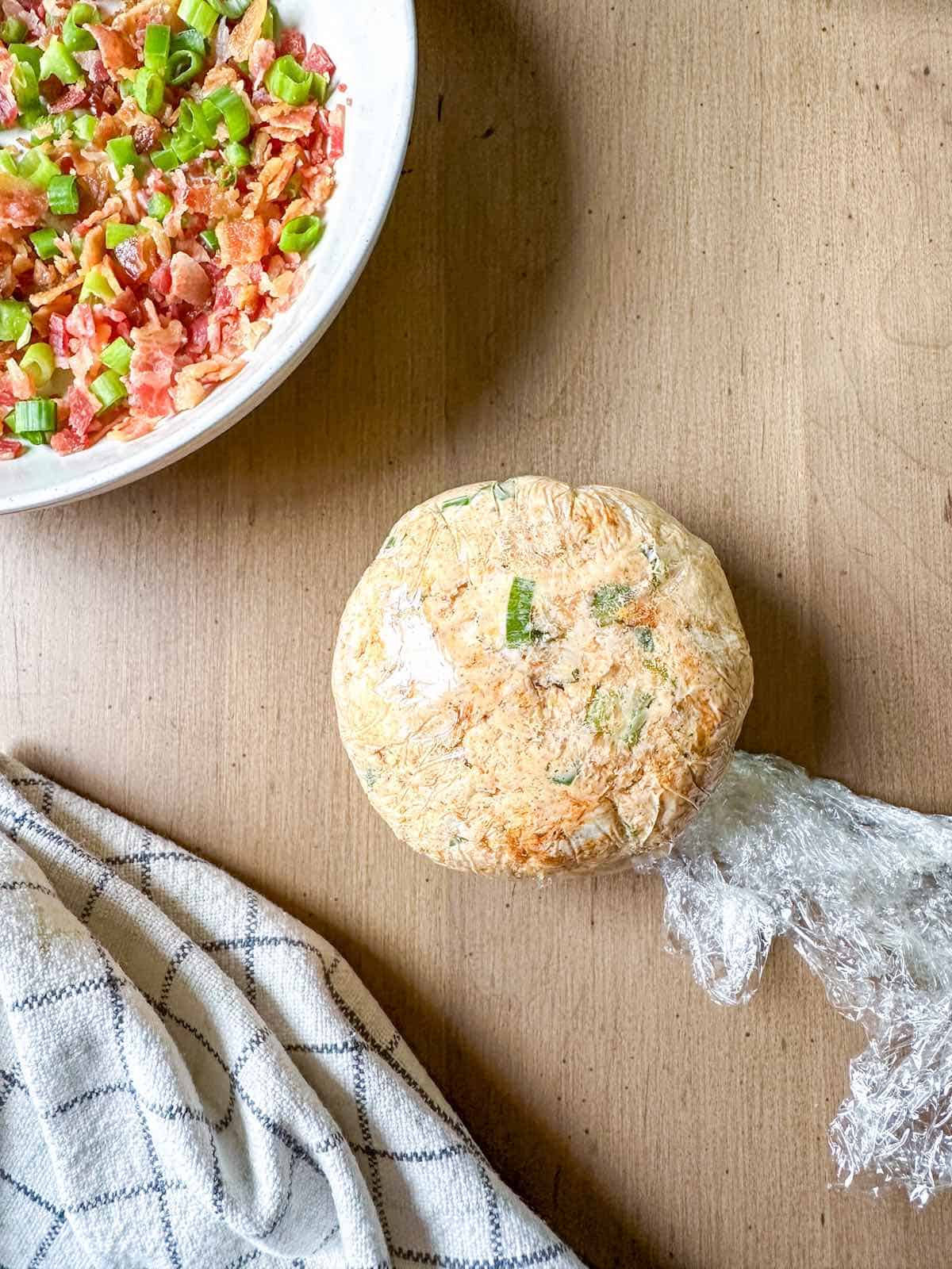 A cheese ball placed in plastic wrap to make in into a sphere.