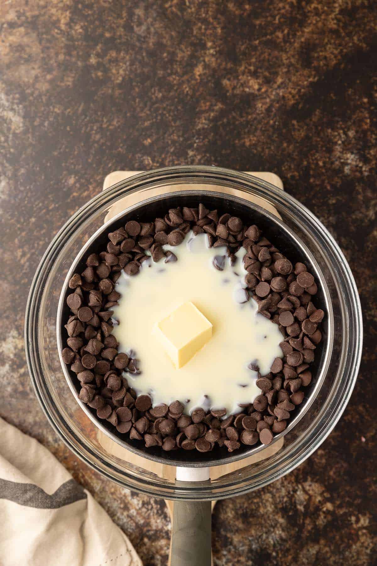 Chocolate chips, condensed milk and butter in a glass bowl on top of a saucepan.