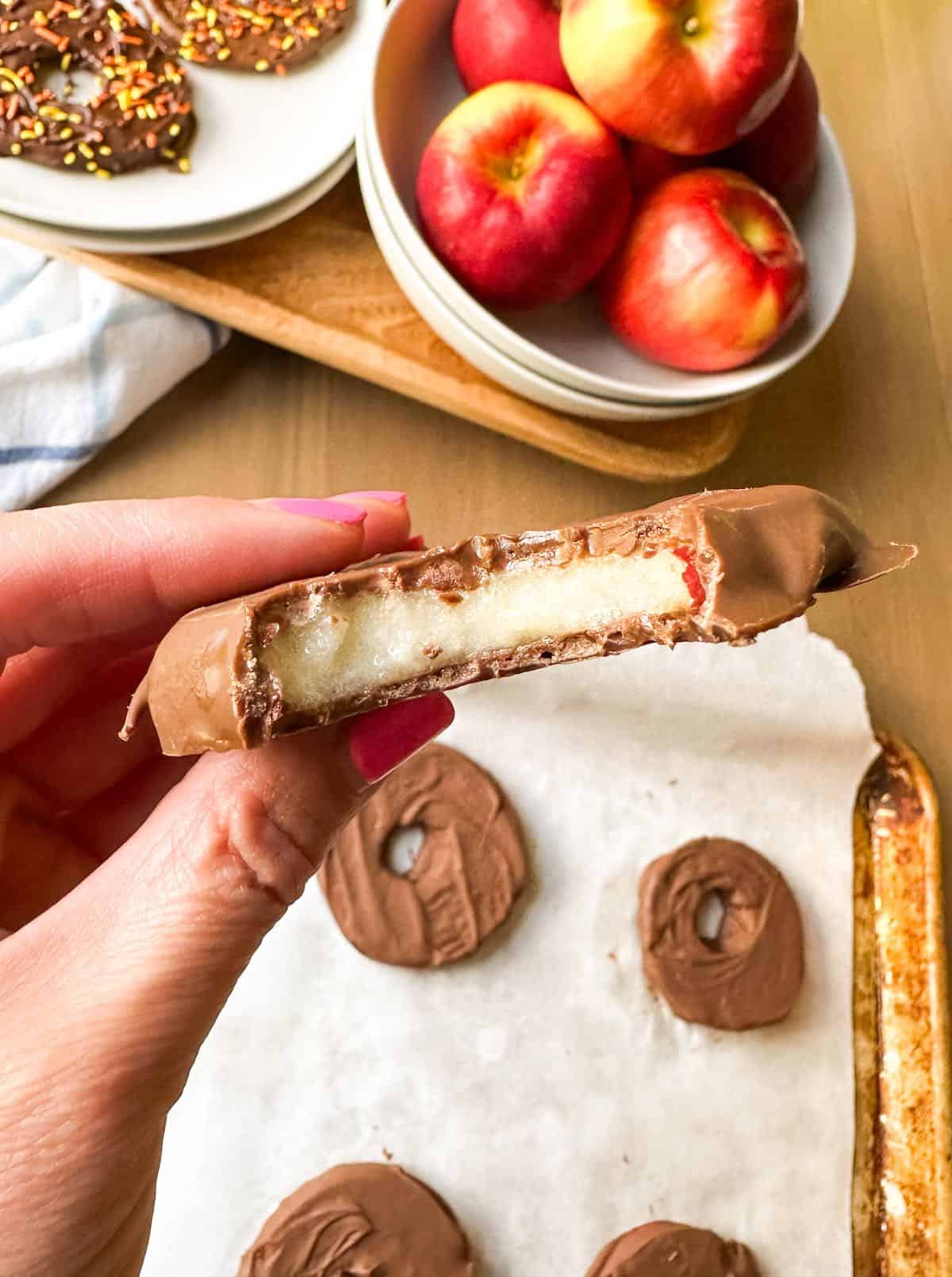 An apple slice coated in chocolate with a bite taken out of it.
