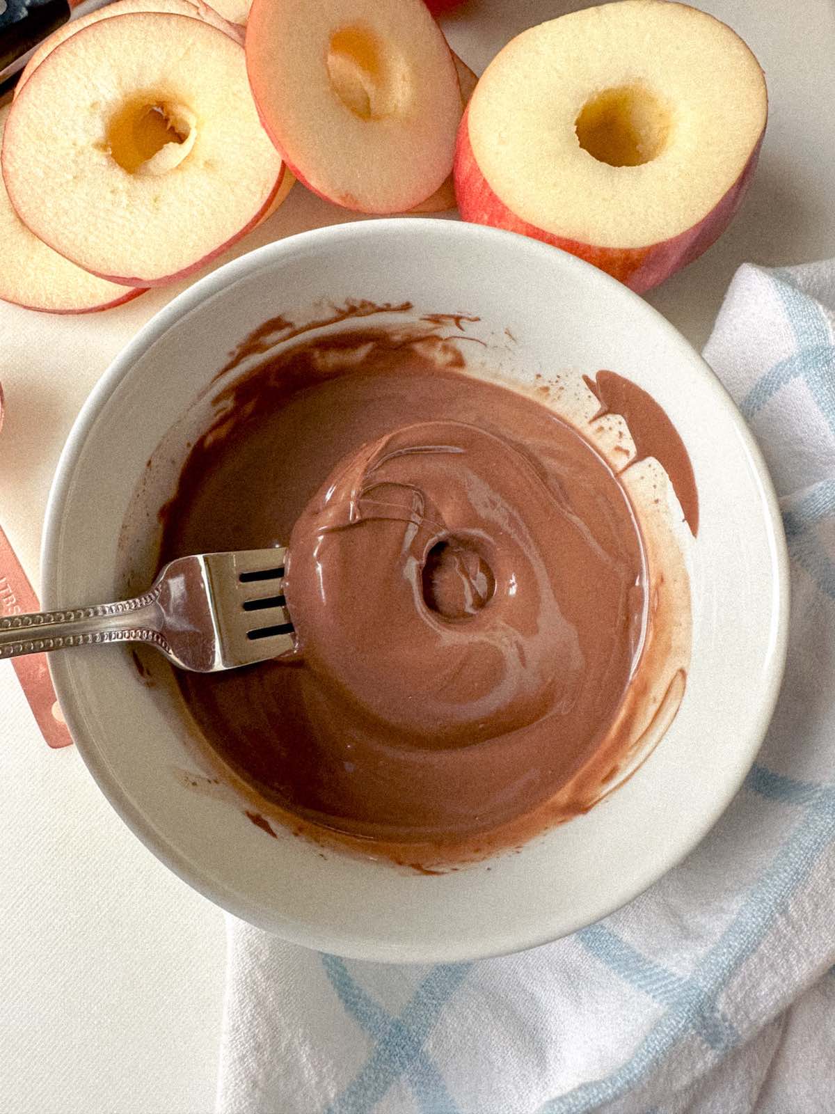 A cored apple circle dipped in a bowl of melted chocolate.