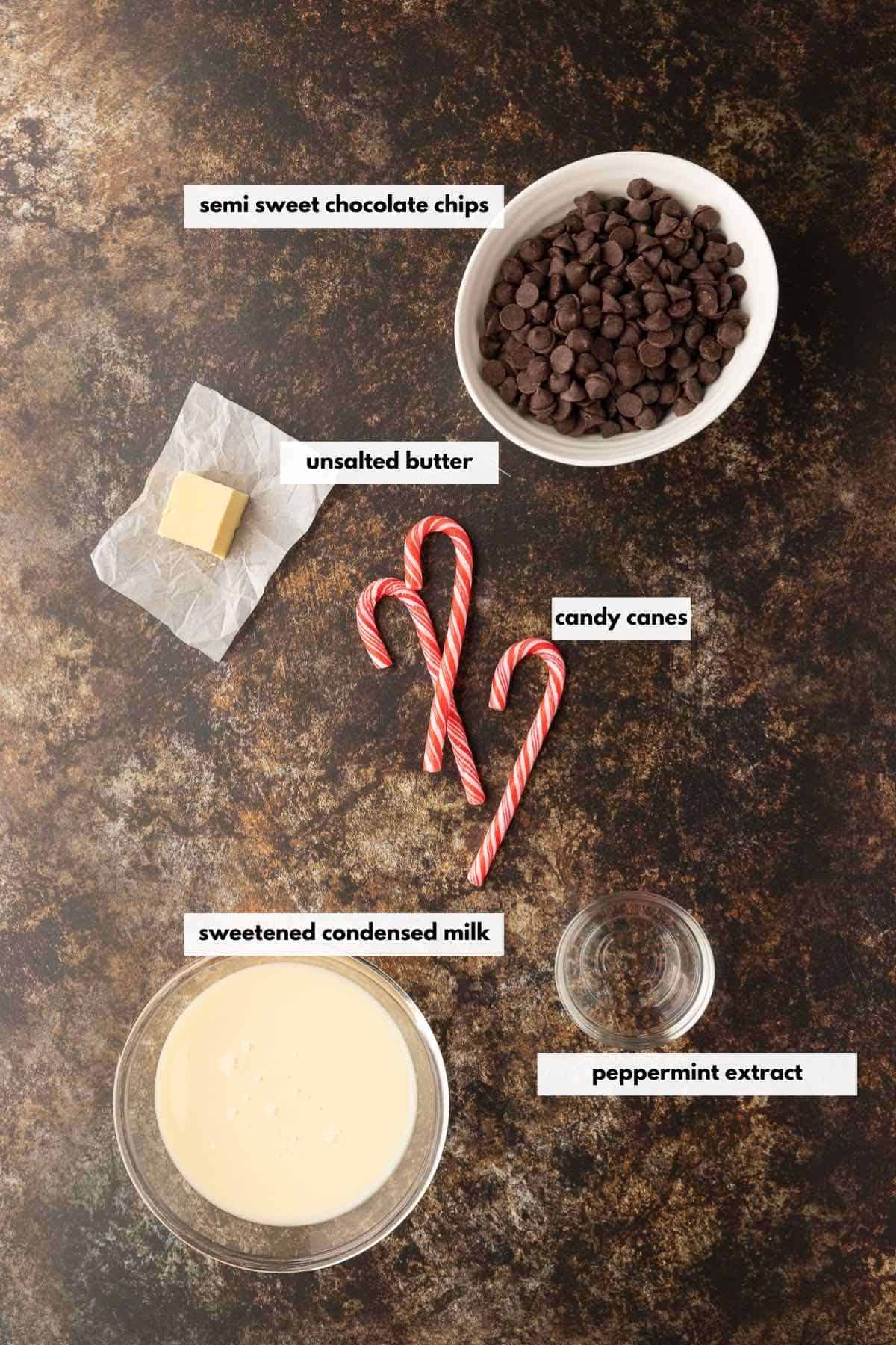 Candy canes, semi-sweet chocolate chips, unsalted butter, peppermint extract, and sweetened condensed milk laid on a table.