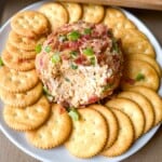 A jalapeno popper cheese ball on a plate surrounded by butter crackers.