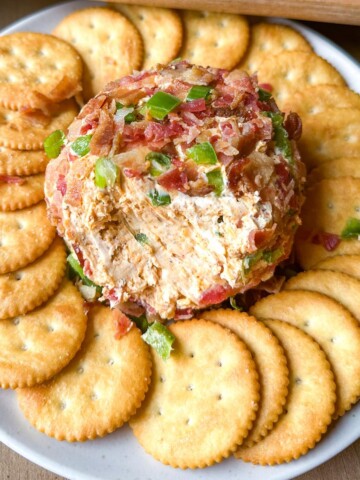 A jalapeno popper cheese ball on a plate surrounded by butter crackers.