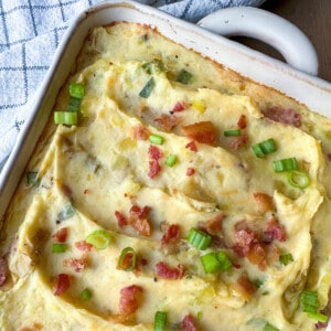 Twice baked potatoes in a casserole dish, topped with cooked bacon bits and green onions.