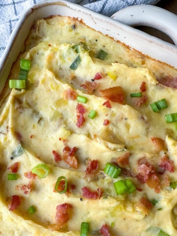 Twice baked potatoes in a casserole dish, topped with cooked bacon bits and green onions.