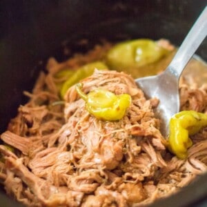 Shredded pork roast on a fork in a slow cooker.