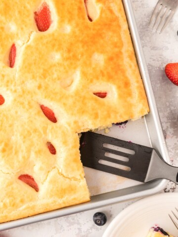 Sheet pan pancakes and berries with a slice cut out.