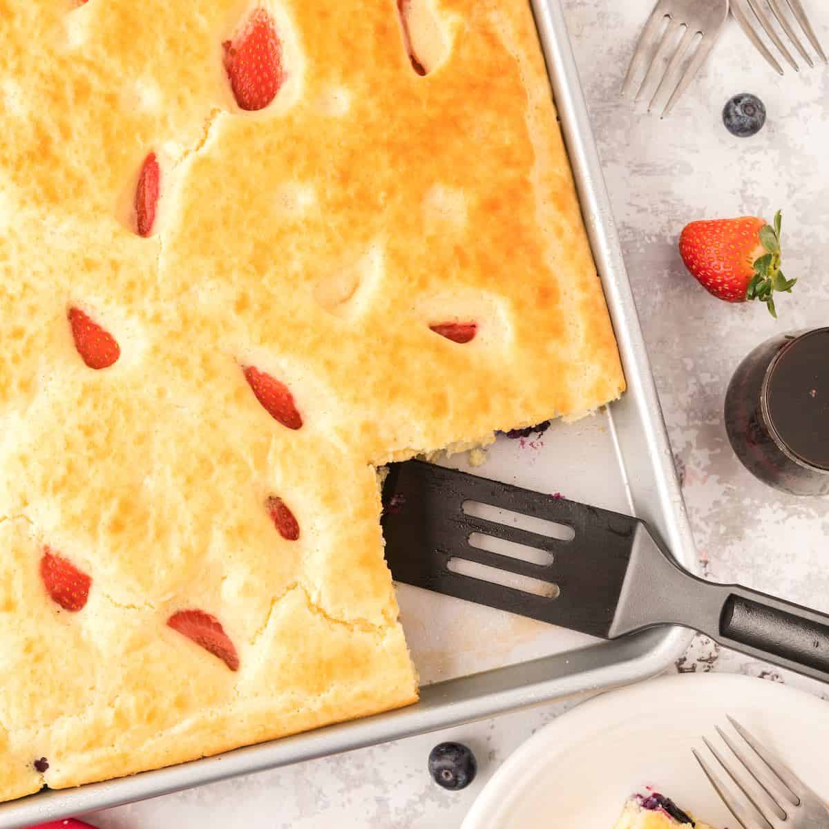 Sheet pan pancakes and berries with a slice cut out.