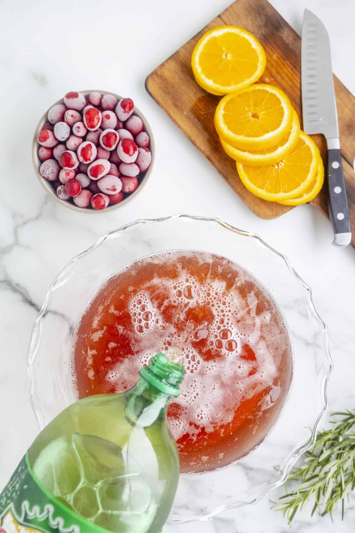 A bottle of ginger ale being poured into a punch bowl.
