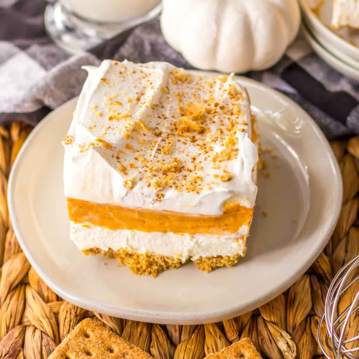 A slice of no bake pumpkin lush dessert on a plate topped with crumbled graham crackers.