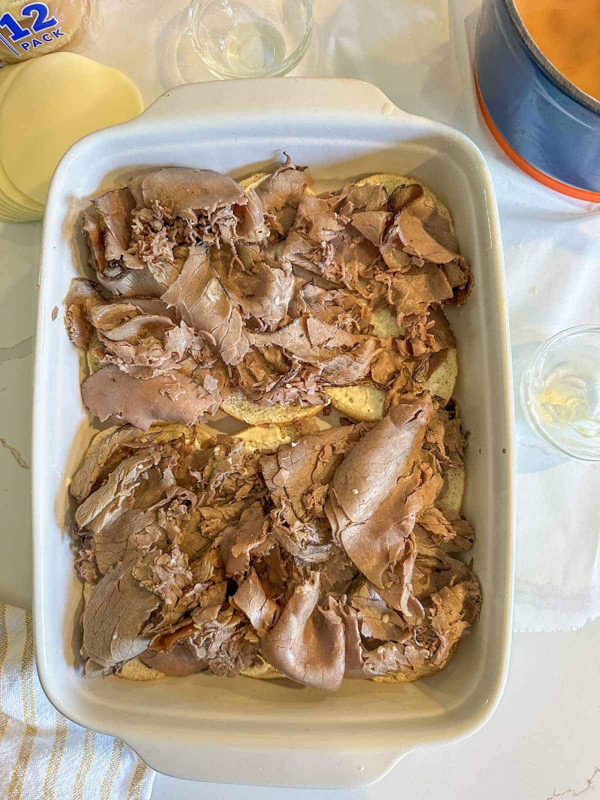 Shaved beef layered over slider buns in a baking pan.