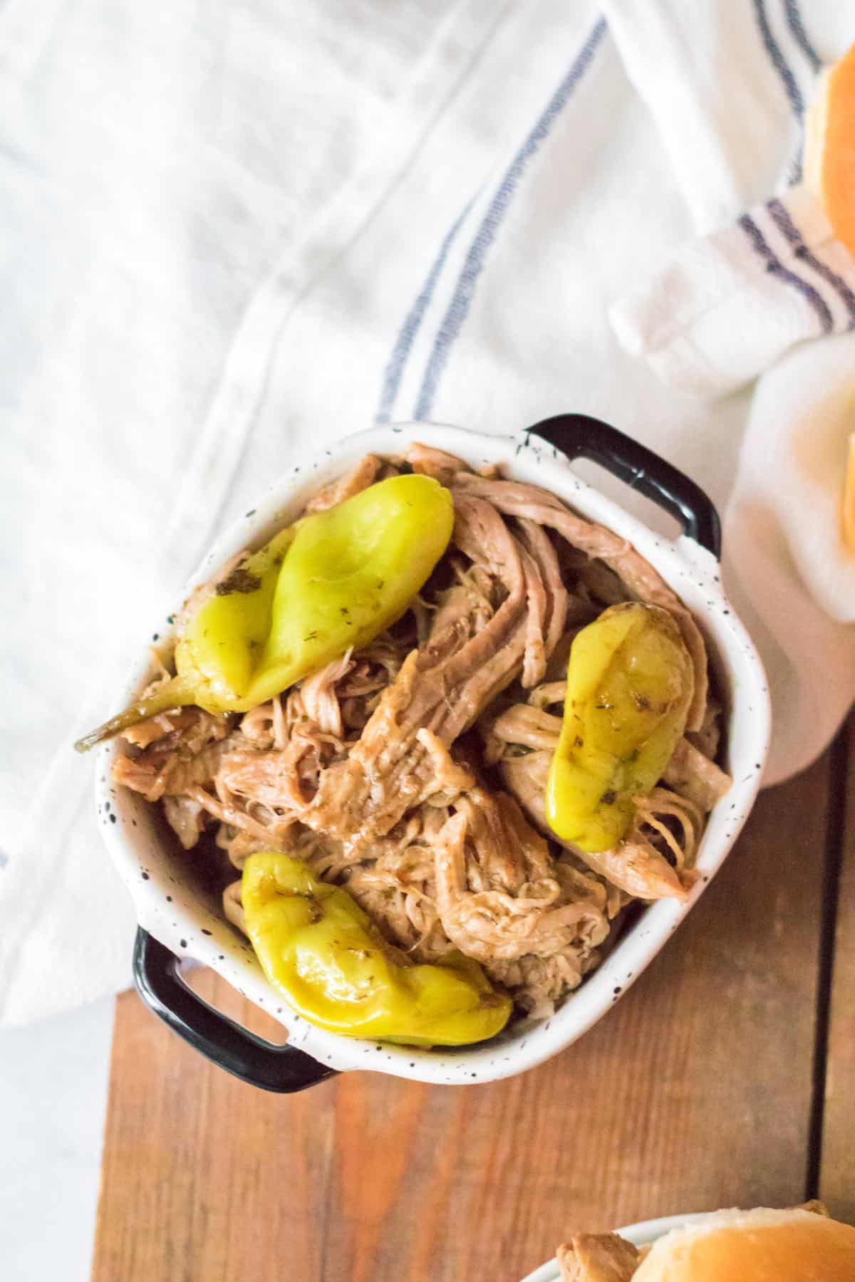 Shredded pork roast with pepperoncini peppers in a square casserole dish.