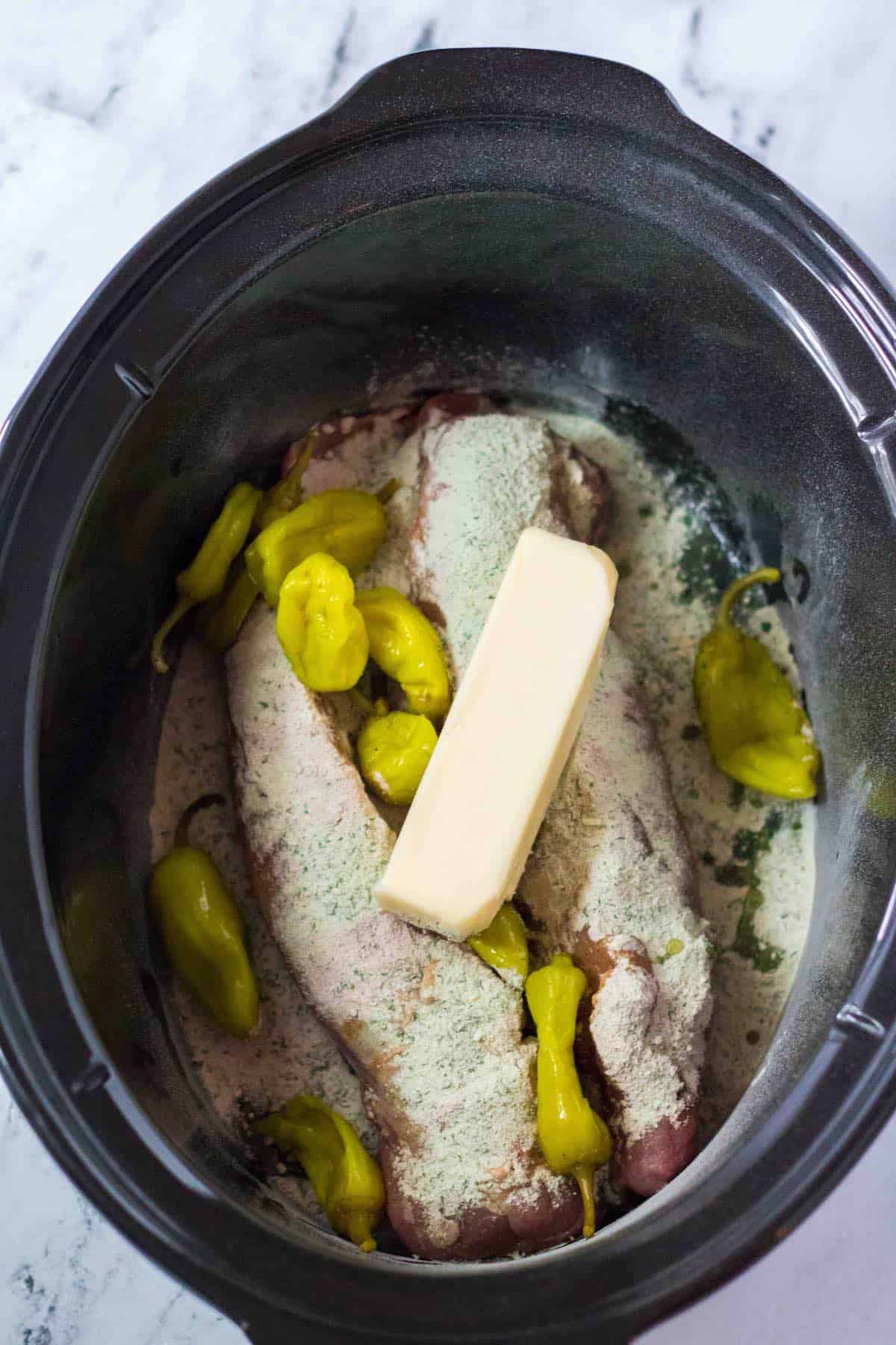 Pork tenderloins in a slow cooker topped with seasonings and a stick of butter.