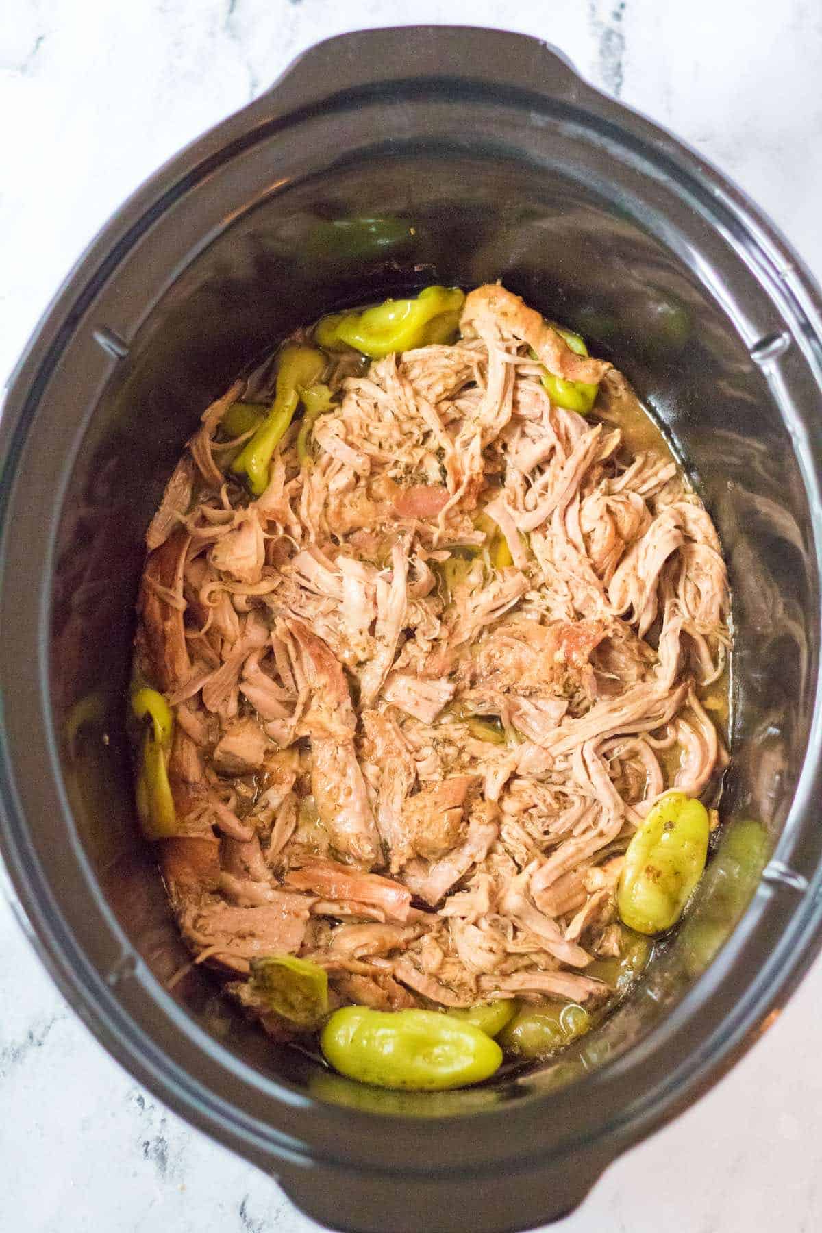 Shredded Mississippi pork roast in juices in an oval crock pot.