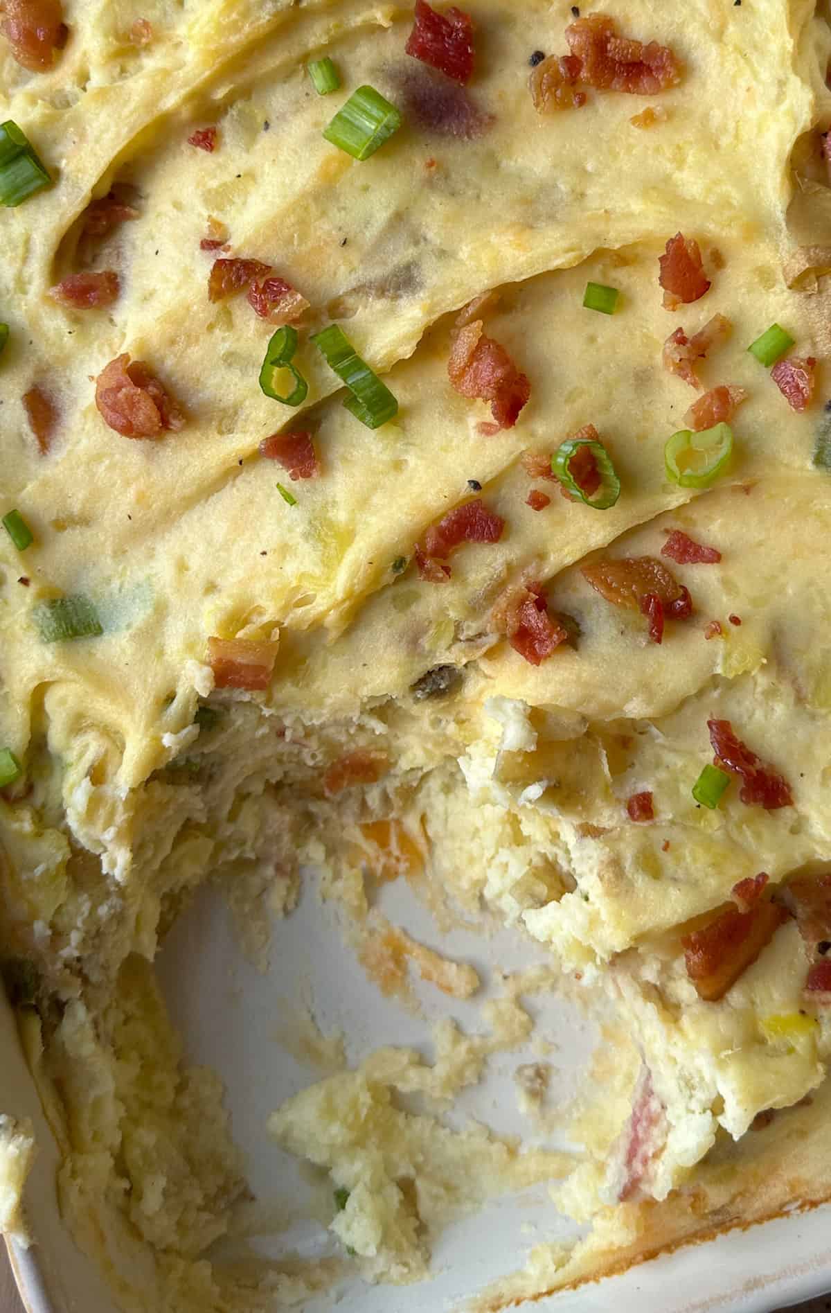 A casserole dish of cheese and bacon mashed potatoes with one portion scooped out.