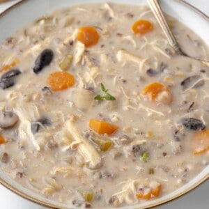 A bowl of creamy chicken soup with carrots, mushrooms and wild rice.