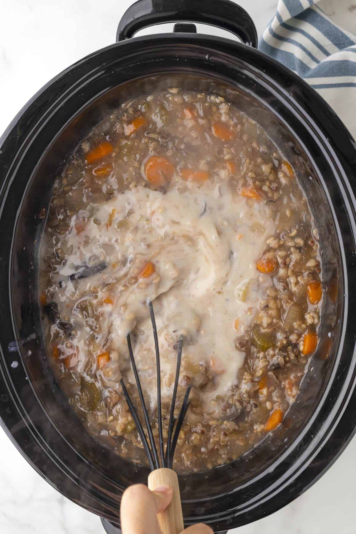 A whisk incorporating a creamy sauce into the chicken wild rice soup.