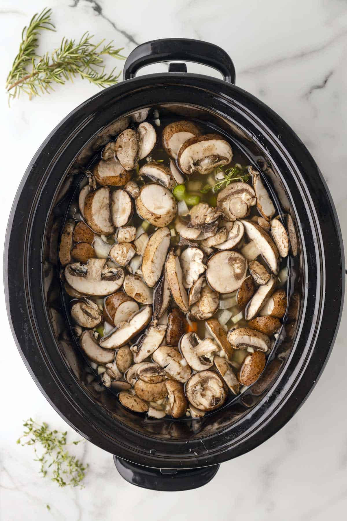 An oval slow cooker filled with mushrooms chicken and wild rice with broth.