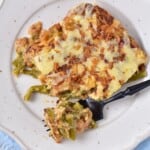 Creamy green bean casserole topped with fried onions and cheese on a plate.