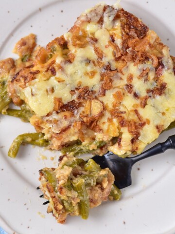 Creamy green bean casserole topped with fried onions and cheese on a plate.