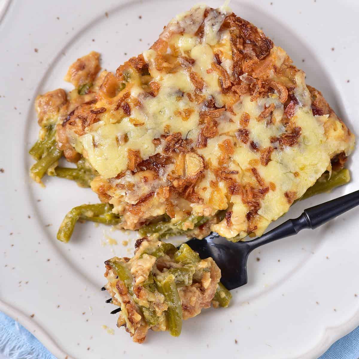 Creamy green bean casserole topped with fried onions and cheese on a plate.
